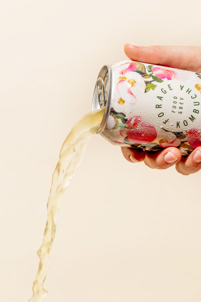 A can of Forage Kombucha being poured out in front of a pale yellow backdrop.